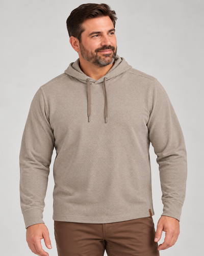 A man wearing a tan Tommy Bahama Fireside Coast Hoodie Big & Tall with a drawstring and brown pants.