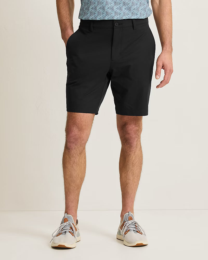 A man faces forward with hands in pockets, wearing black Tommy Bahama Barbados Shorts Big & Tall, a patterned short-sleeve shirt, and white sneakers.