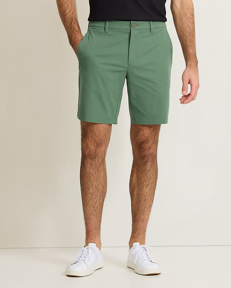 A man stands against a plain background with his hands in his pockets, wearing Tommy Bahama Barbados Shorts Big & Tall in green, a black shirt, and white sneakers.