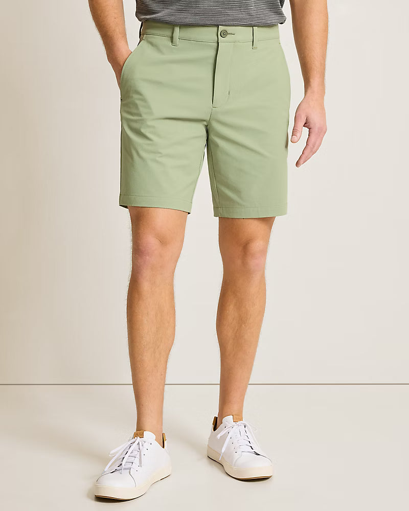 A person wears Tommy Bahama Barbados Shorts Big & Tall in light green, paired with a gray striped shirt tucked in and white sneakers, standing against a neutral background.