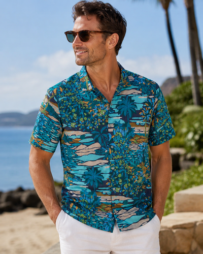 A man in sunglasses, white pants, and a Tori Richard Printed Cotton Opalescent Shirt (1956M0330) stands outdoors by the beach with palm trees in the background.