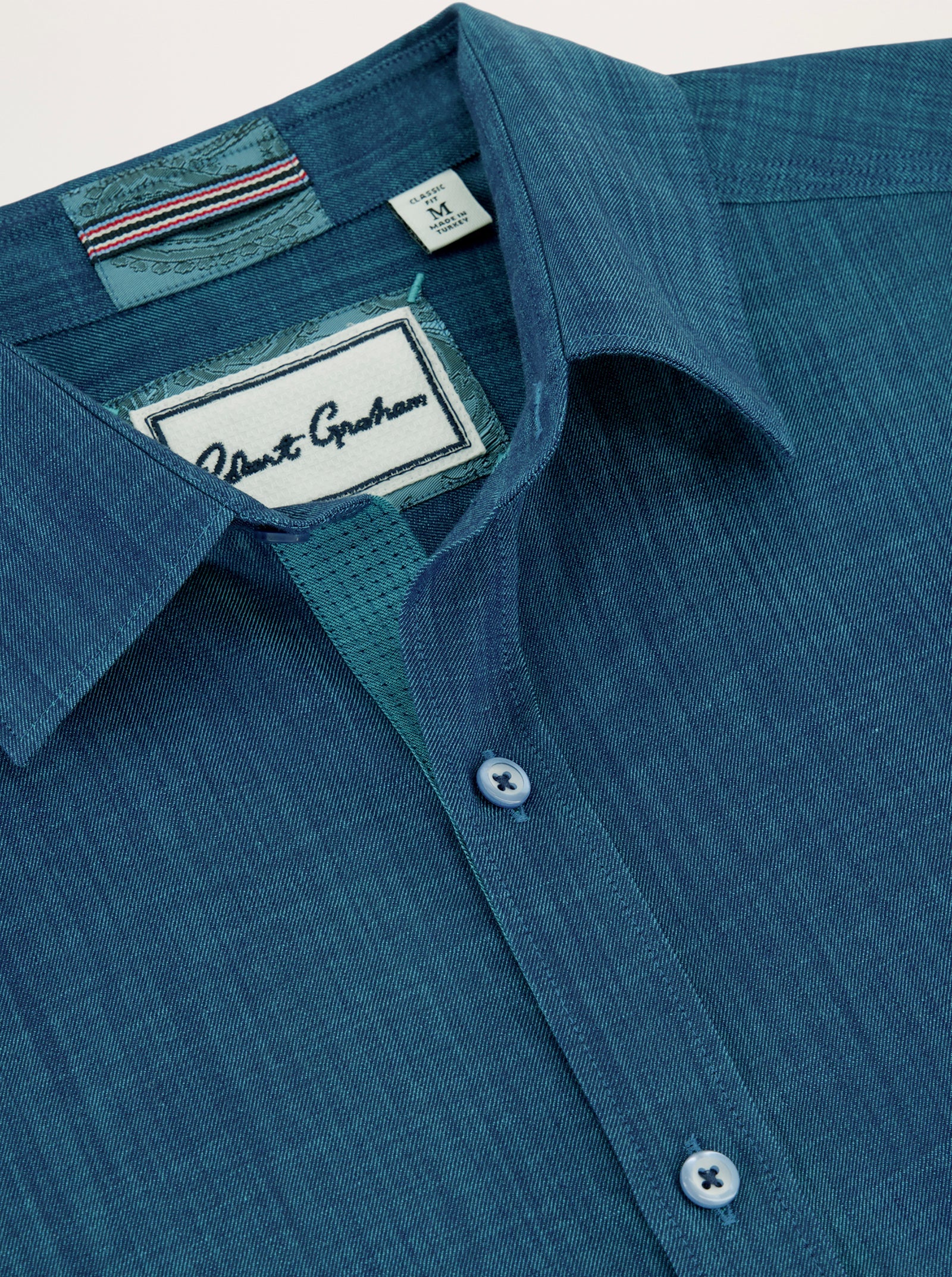 Close-up of the Robert Graham Kerrington Woven Shirt Big & Tall, featuring a blue textured weave, pointed collar, two matching blue buttons, and a visible Robert Graham label inside the collar. This stylish shirt from the Robert Graham Big & Tall collection highlights the refined details of a two-tone chambray design.