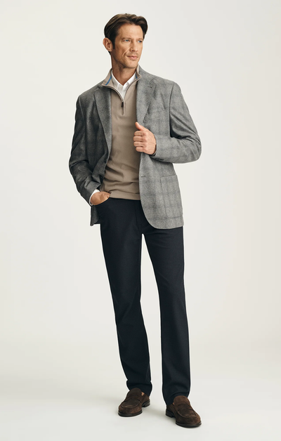 A man wearing the 34 Heritage Courage Supreme Plaid blazer by 34 Heritage, paired with a beige pullover, white collared shirt, black pants, and brown shoes stands with one hand in his pocket.