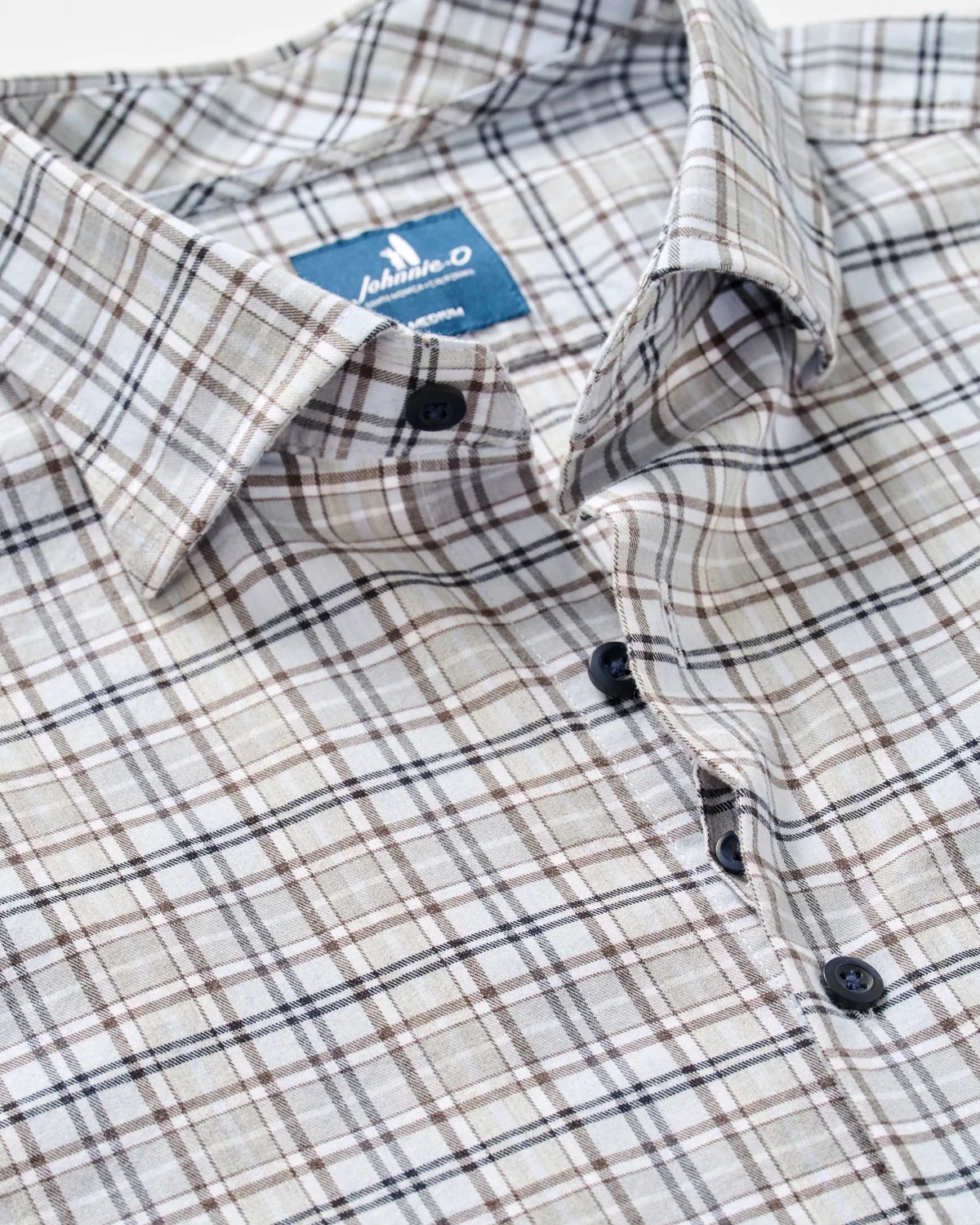 Close-up of a buttoned, long-sleeve men’s flannel shirt from Johnnie-O, featuring a beige, brown, and black plaid pattern and a visible blue label inside the collar. The Johnnie-O Tahoe Plaid Flannel Shirt Big & Tall offers a classic yet modern look.