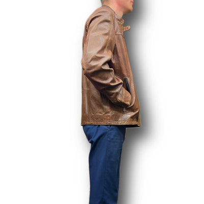 A person in profile stands against a white background, wearing the Missani Leather Jacket 392834 made of rich brown Italian lambskin and blue pants, with one hand in their pocket.