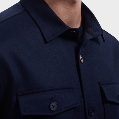 Close-up of a person wearing the Bugatchi Button Shirt Jacket KX9015JS1, a dark navy shirt by Bugatchi featuring two front flap pockets and a classic collar. This wrinkle-resistant shirt jacket combines style and comfort, making it perfect for everyday wear.