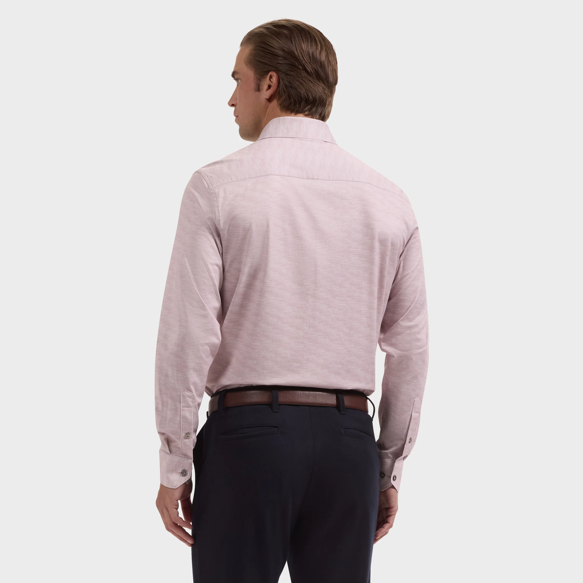 A man stands with his back to the camera, wearing a light pink Bugatchi James Herringbone Sport Shirt (KF9508K60) and dark trousers against a plain background.