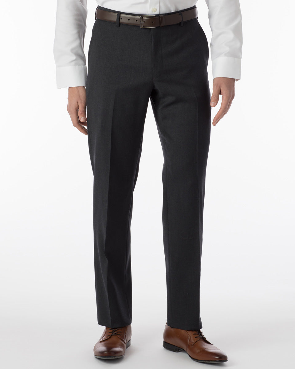 A person wearing Ballin Super 120's Comfort-EZE Big & Tall charcoal trousers, a white shirt, a brown belt, and brown dress shoes stands against a plain white background.
