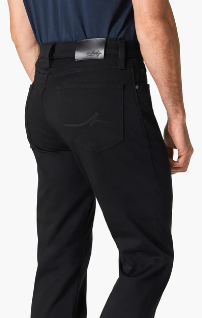 A person is seen from the back wearing 34 Heritage Charisma Double Black pants and a navy shirt, highlighting the rear pocket details and a silver 34 Heritage label on the waistband.