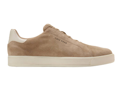 The Cole Haan GrandPro Luxe Slip On Sneaker features a tan suede upper, breathable design, white rubber sole, and Cole Haan branding on the side, displayed in a side profile against a white background.