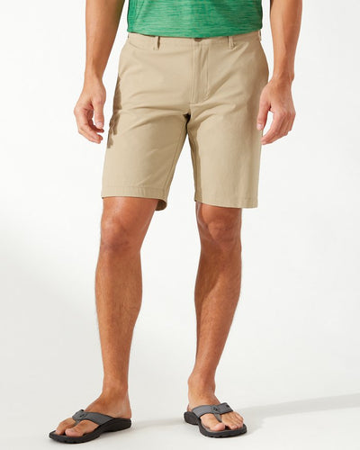 A person wearing a green shirt, black flip-flops, and Tommy Bahama Chip Shot Shorts Big & Tall by Tommy Bahama with UPF 30 protection stands against a plain background.