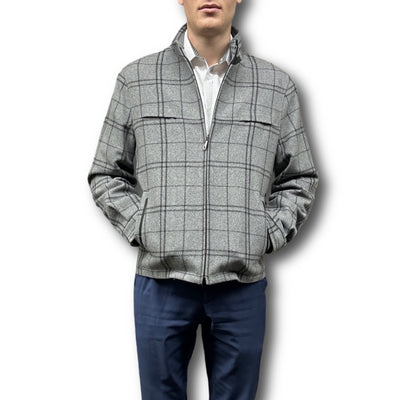 A man stands against a white background wearing the Enzo Coat Play by Enzo—a gray plaid luxury zip-up jacket with hands in pockets, paired with a white shirt underneath and navy blue pants.