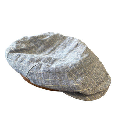 The Wigens Linen Ivy Cap 90483 by Wigens is a light gray plaid flat cap with a short curved peak, subtle white lines, and a narrow shaped crown, shown from an angled side view on a white background.