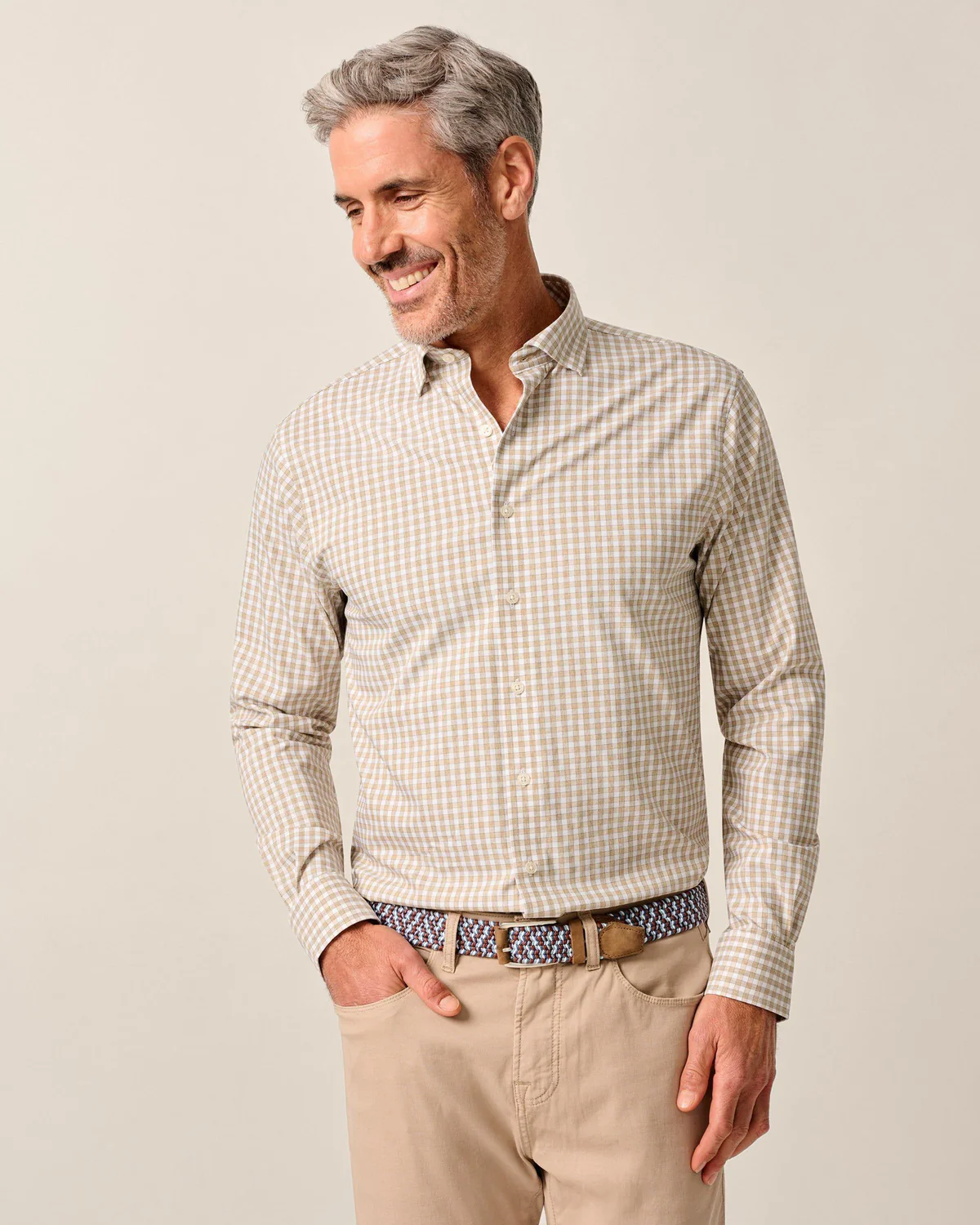 Man with gray hair, wearing the Johnnie-O Westwood Performance Check Shirt and beige pants, stands with one hand in his pocket and smiles.