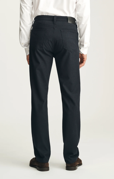 A person is shown from the back, wearing the 34 Heritage Courage Supreme Plaid trousers by 34 Heritage, paired with a white dress shirt and brown shoes, standing against a plain light background.