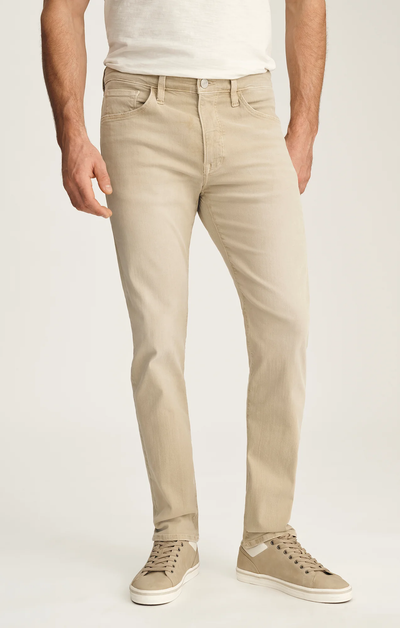 A person wearing 34 Heritage Courage Jeans Urban by 34 Heritage, a white t-shirt, and beige sneakers stands against a plain light background.