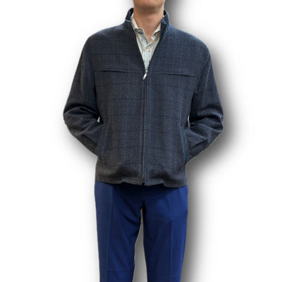 A person in a dark grey zip-up jacket with a subtle check pattern and blue pants stands against a white background, embodying the refined style of Enzo’s luxury outerwear, such as the Enzo Coat Play.
