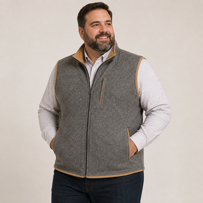 A man wearing the F/X Fusion Melton Vest Big & Tall 13010 over a plaid button-down shirt stands with his hands in his pockets, looking to the side and smiling.