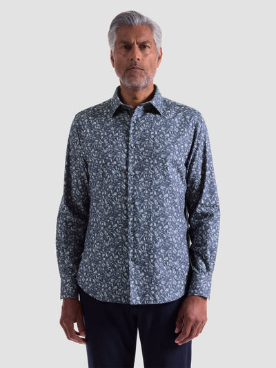 A man stands facing forward against a plain light gray background, wearing the Bugatchi Julian Woven Sport Shirt HS3051L3S in blue floral cotton and dark pants.