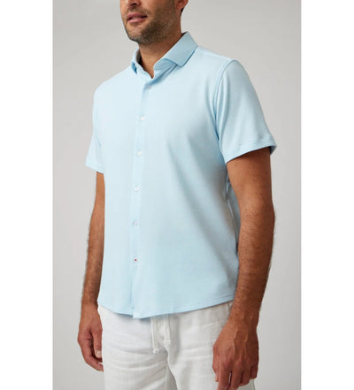 Man in a Stone Rose SS Pique Shirt 2K7T241 (light blue, short sleeve) and white pants, standing against a plain light gray background.