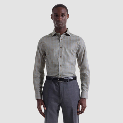 A man faces forward wearing the Bugatchi Axel Grid Sport Shirt HS3285L7S— a patterned long-sleeve shirt with a spread collar—paired with grey trousers and a black belt, set against a plain light background.