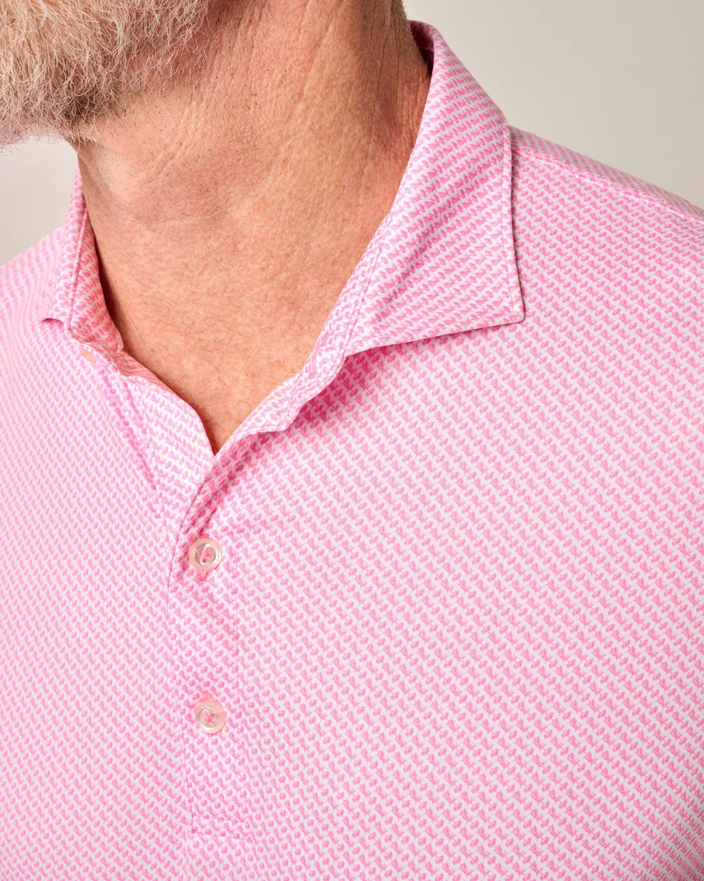 Close-up of a man’s neck and upper chest wearing the Johnnie-O Performance Polo - Wesson, a light pink patterned collared shirt with buttons from Johnnie-O, designed for cool comfort.