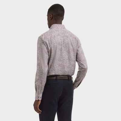A man stands facing away against a plain background, wearing the Bugatchi James Abstract Sport Shirt KF9300K60—an abstract-patterned long-sleeve shirt by Bugatchi—tucked into dark pants with a black belt.