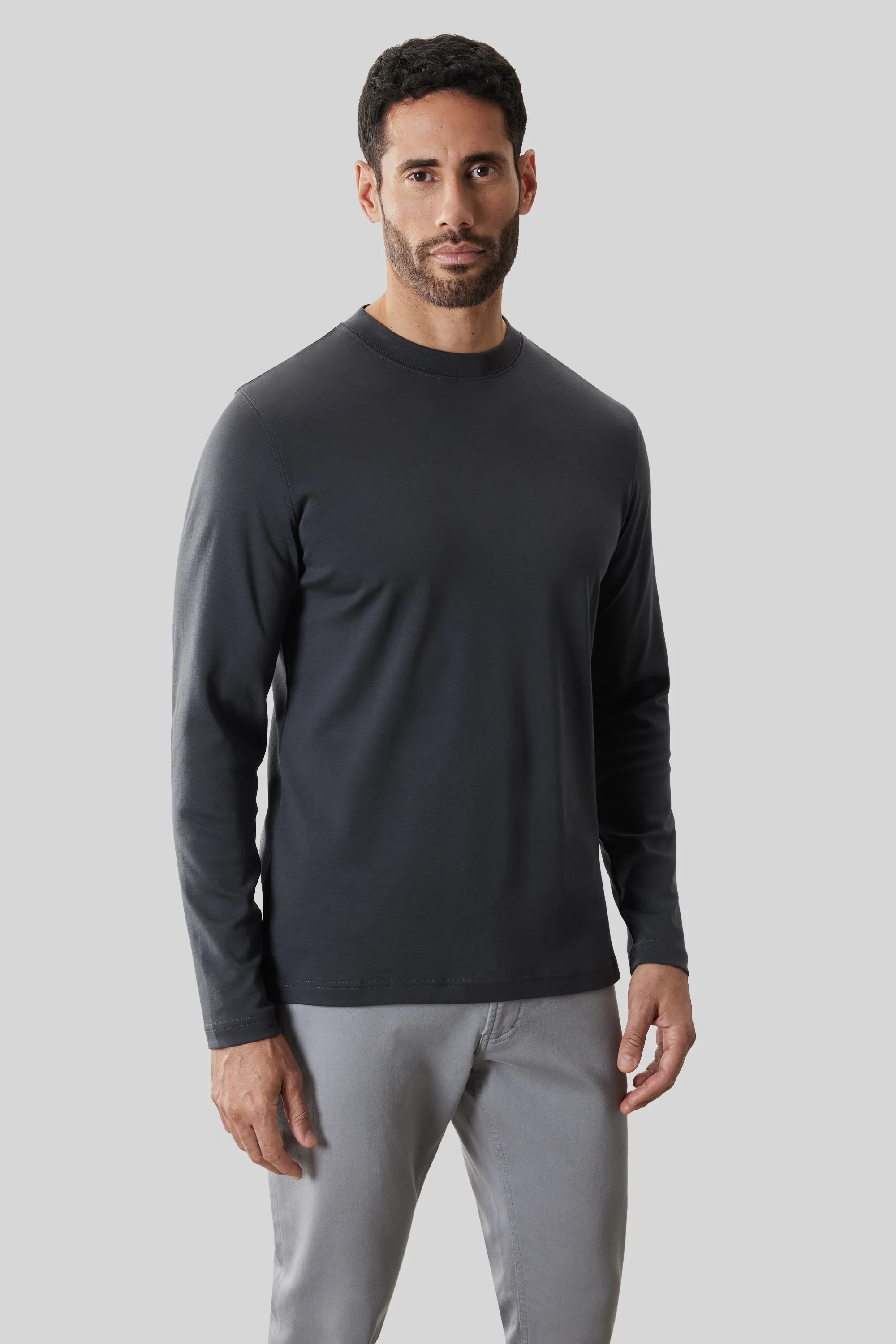 A man wears a Robert Barakett High Crew Long Sleeve RB82247 in dark gray and light gray pants, standing against a plain light gray background.