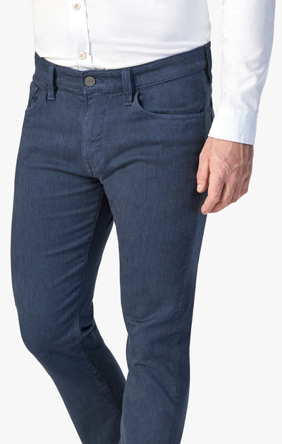 A man wears a white button-up shirt and 34 Heritage Charisma Diagonal Big&Tall jeans by 34 Heritage, with his right hand resting by his side.