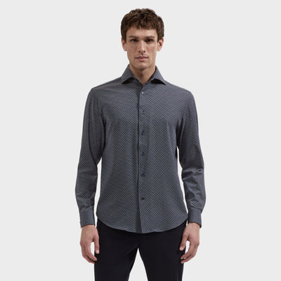 A man stands against a plain background, wearing the Bugatchi Devon Geometric Sport Shirt (KF9431K80)—a long-sleeve, button-up shirt crafted from wrinkle-resistant OoohCotton® performance fabric featuring a subtle geometric pattern—paired with dark pants for a polished look that lasts all day.