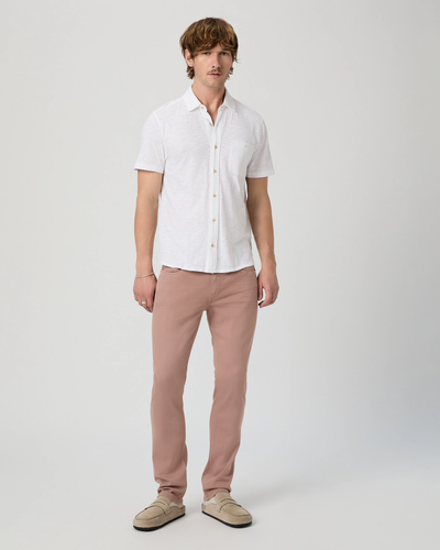 A man stands against a plain background wearing a white short-sleeve button-up shirt, Paige Federal Slim Straight Jeans by Paige, and beige loafers.