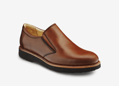 The Samuel Hubbard Frequent Traveler Black 10 is a black slip-on shoe by Samuel Hubbard, featuring a black rubber sole, light stitching along the edge, and a cushioned memory foam insole, displayed on a white background.