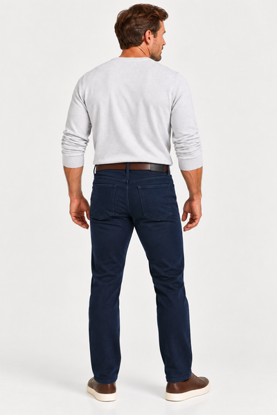 Man standing with his back to the camera, wearing a light gray top, Alberto PIPE 1607 Diamond Brushed Stretch Cotton Jeans, brown belt, and sneakers against a white background.