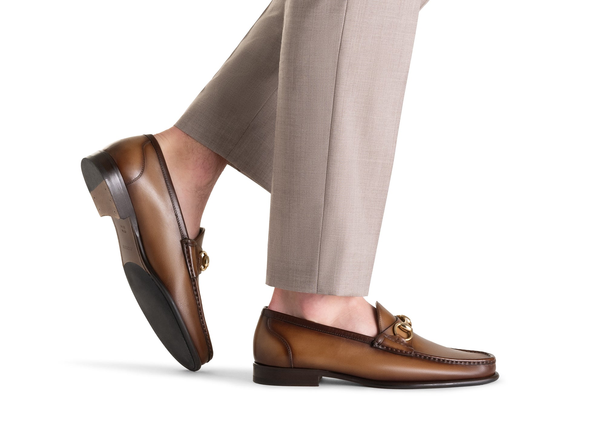 A person wearing light beige dress pants, one foot slightly raised, showcases the Magnanni Giancarlo Moc Toe Bit Loafer: brown calfskin and suede loafers by Magnanni, adorned with gold hardware and subtle hand-stitched accents.