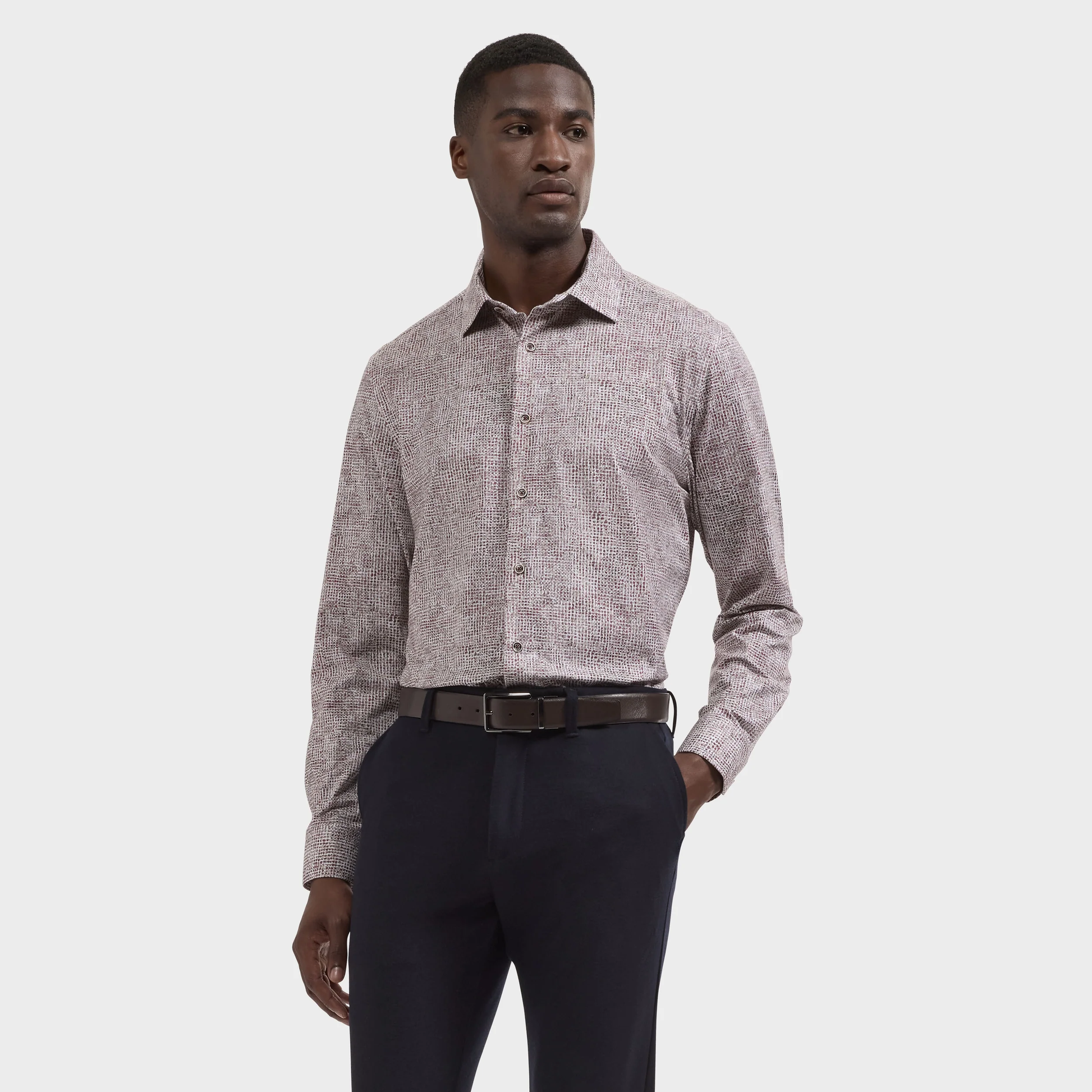 A man stands against a plain background wearing the Bugatchi James Abstract Sport Shirt KF9300K60, paired with dark trousers and a black belt.