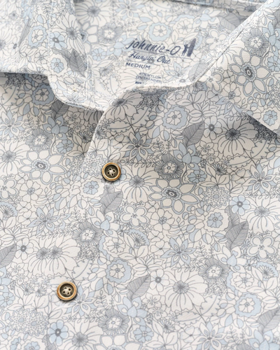 Close-up of the Johnnie-O Kayce Big&Tall Short Sleeve shirt, featuring a light blue and white floral pattern, two beige buttons, and a visible Johnnie-O label inside the collar for laid-back, untucked style.