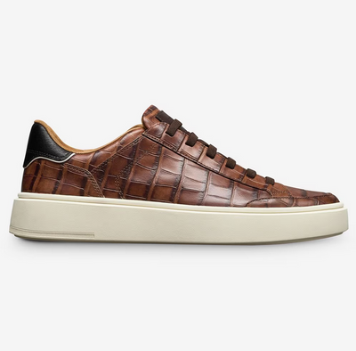 The Allen Edmonds Oliver Sneaker features premium brown crocodile-embossed leather, a white rubber sole, brown laces, and a black heel accent. Designed by Allen Edmonds for stylish comfort and support on any journey. Shown in side view.