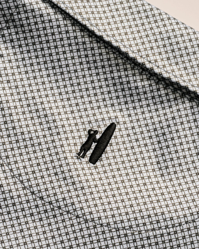 Close-up of the Johnnie-O Link Big & Tall Performance Jersey Polo collar, showing a small embroidered person with a surfboard on its patterned performance jersey fabric.