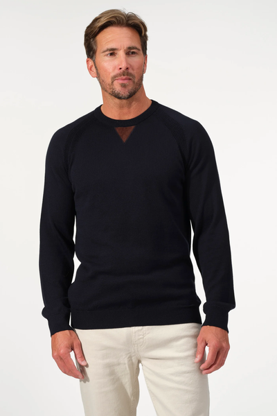A man stands against a plain white background wearing the Garnet Milano Crew Sweater 2522003CS in black, crafted from luxurious Italian yarn, paired with beige pants.
