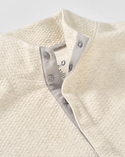 Close-up of the Johnnie-O Ransel Hidden Snap Pullover Big & Tall, featuring a cream drirelease stretch fabric, a grey inner placket, and two partially unfastened metal snaps that reveal part of the collar tag.