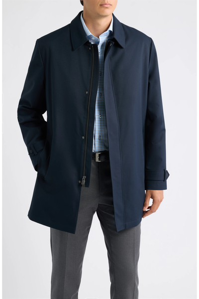 Man wearing a dark navy Hart Schaffner Marx Milo Waterproof All-Weather Jacket over a blue plaid button-down shirt and grey trousers.