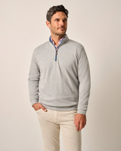 A man stands at an angle against a plain background, wearing a Johnnie-O 1/4 Zip Sweater SULLY Big & Tall over a collared shirt and beige pants, with one hand in his pocket.