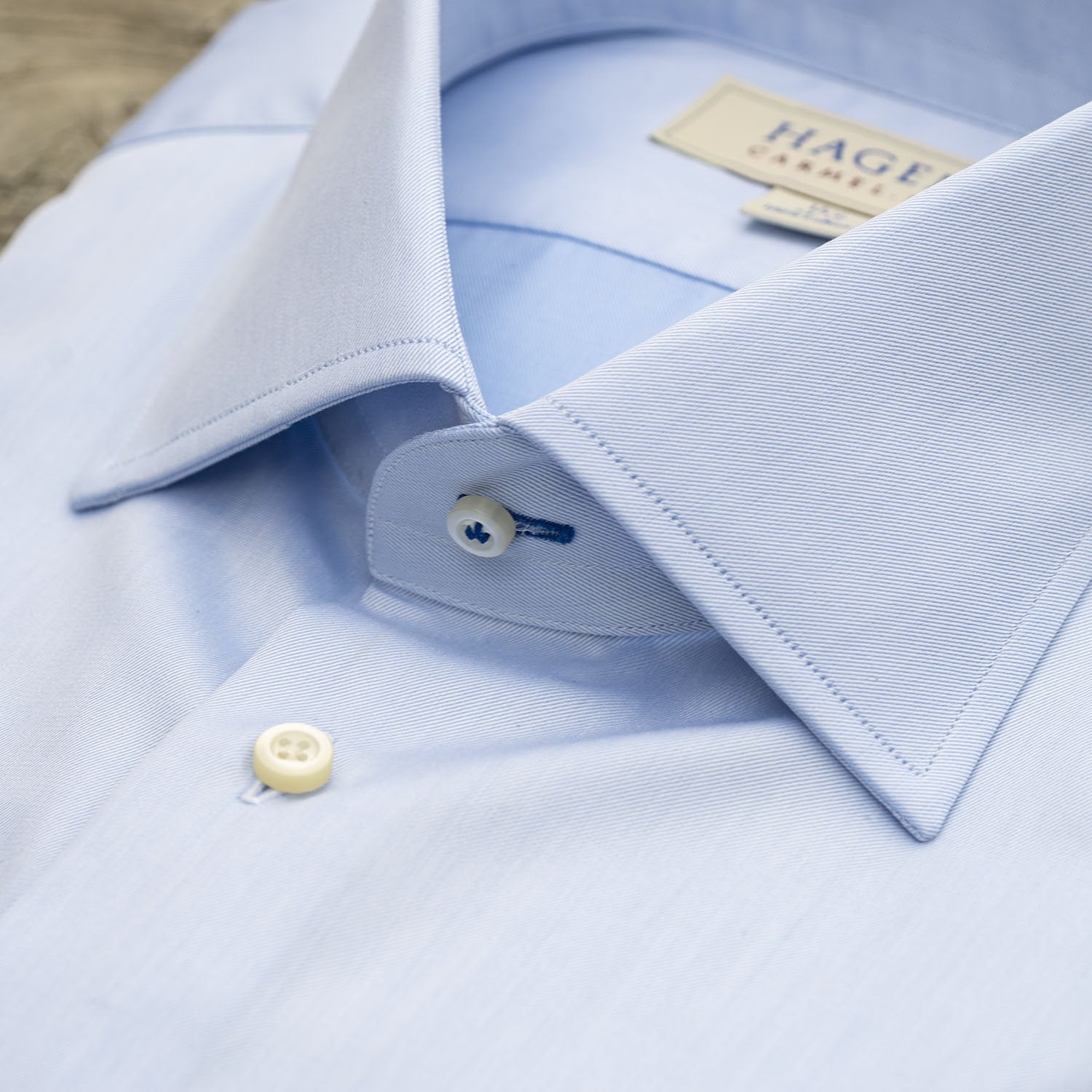 Close-up of the Hagen Solid Twill Shirt MB1864400 by Hagen—a neatly folded blue dress shirt made from superfine twill 100% cotton, featuring a pointed collar and white buttons, displayed on a wooden surface.