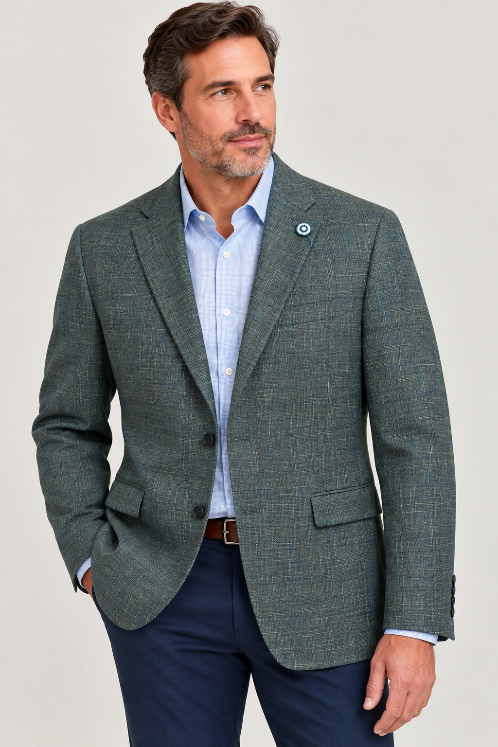 A man wearing a Hart Schaffner Marx Olive Sport Coat New York Fit 35H0132, expertly tailored and paired with a light blue dress shirt and navy pants, stands with one hand in his pocket while looking to the side against a neutral background.