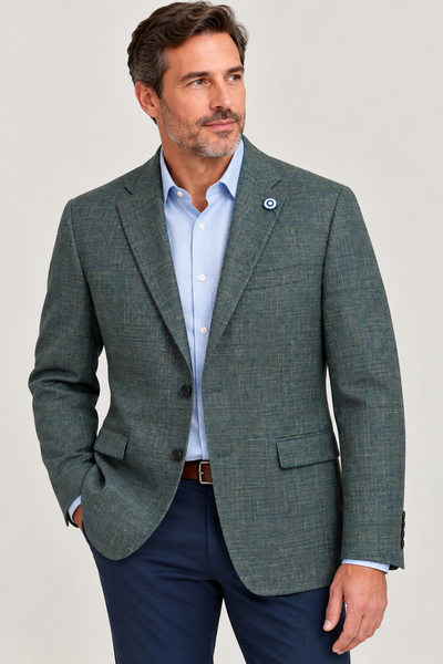 A man wearing a Hart Schaffner Marx Olive Sport Coat New York Fit 35H0132, expertly tailored and paired with a light blue dress shirt and navy pants, stands with one hand in his pocket while looking to the side against a neutral background.