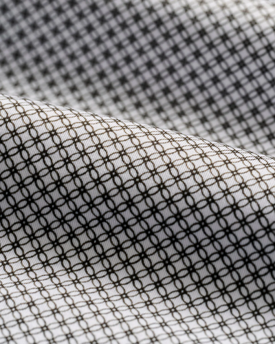 Close-up of the Johnnie-O Link Big & Tall Performance Jersey Polo by Johnnie-O, featuring white fabric with a black geometric circle pattern. This golf polo material is slightly draped and provides UPF 50 sun protection.
