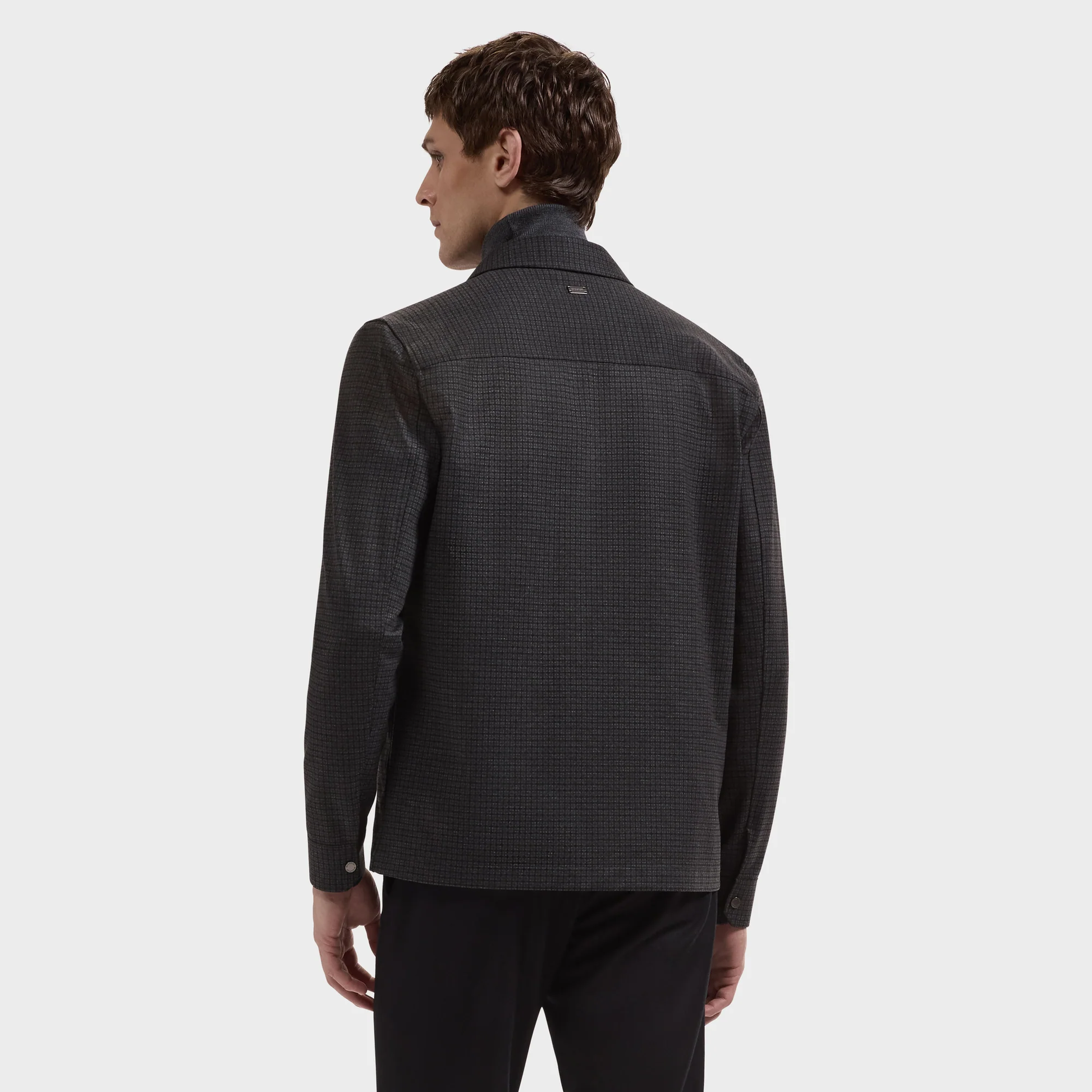 A man stands facing away, wearing the Bugatchi Micro Check Knit Shirt KF2313K93—crafted from performance stretch fabric—paired with black pants, set against a plain light gray background.