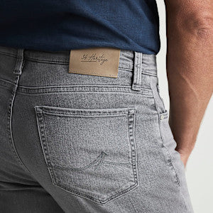 A person wearing 34 Heritage Courage Jeans Urban—light gray, straight leg jeans from 34 Heritage crafted from premium Urban denim—and a dark blue shirt, with a tan label on the waistband above the back pocket.