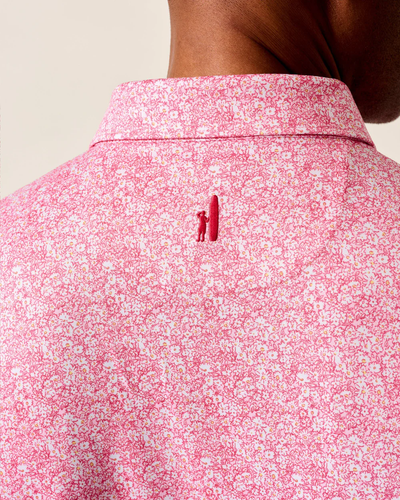 Close-up of the back of a person's neck and shoulders wearing the Johnnie-O Performance Polo- Wildflower by Johnnie-O, featuring a small embroidered figure and surfboard below the collar. This lightweight polo also offers UPF 50 sun protection.
