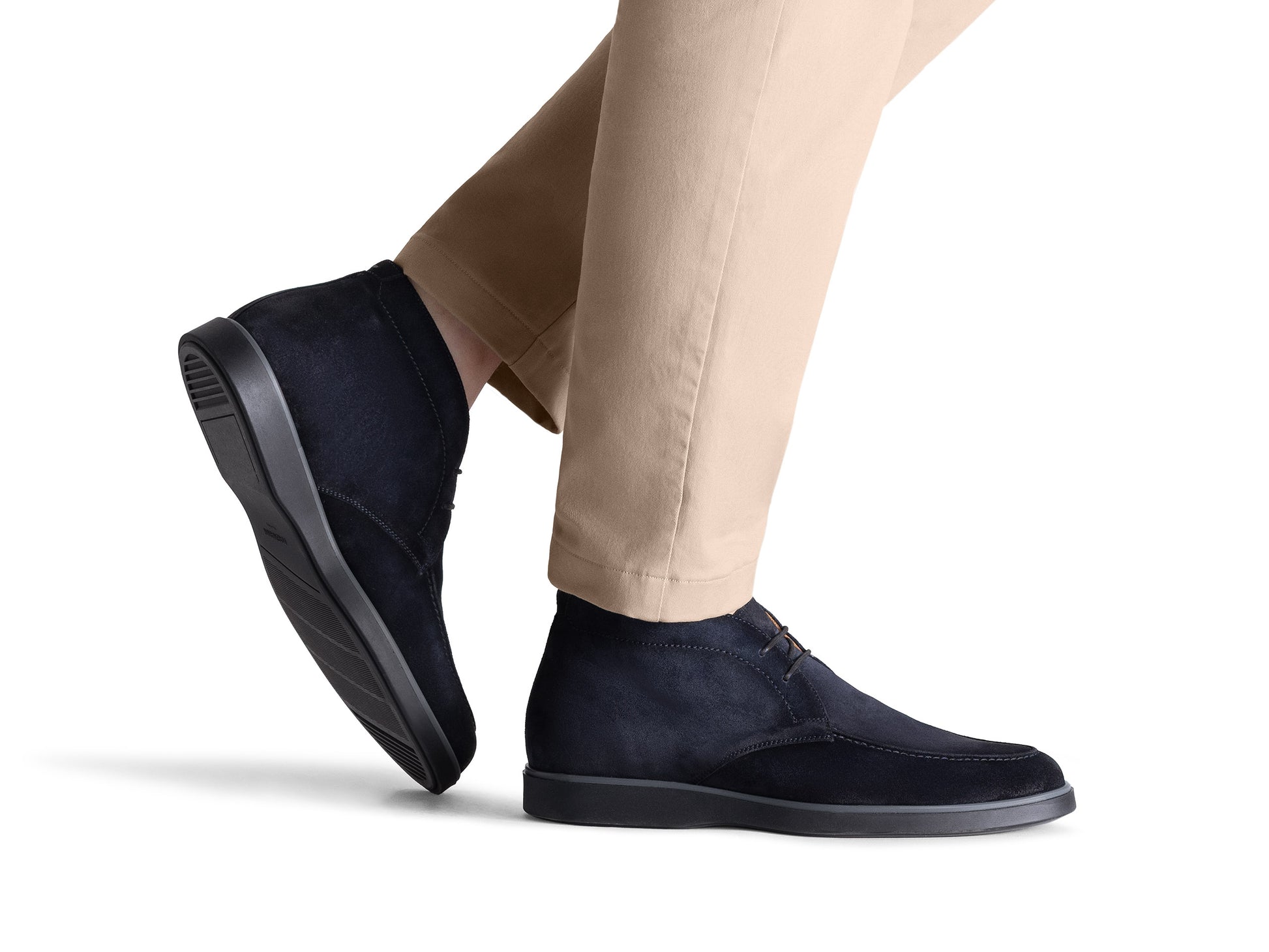 A person wearing beige pants and Magnanni Lello Suede Chukka Boots, featuring black suede uppers and rubber soles by Magnanni, is shown from the lower legs against a white background.